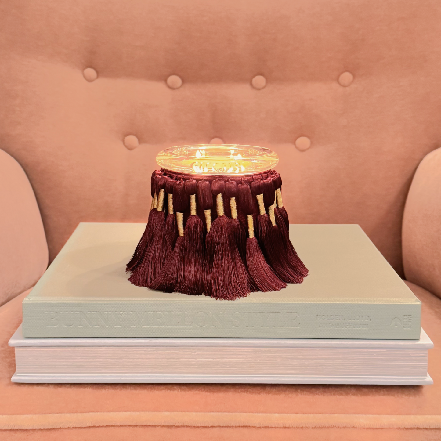 circus candle with tassels on a stack of books against a pink background