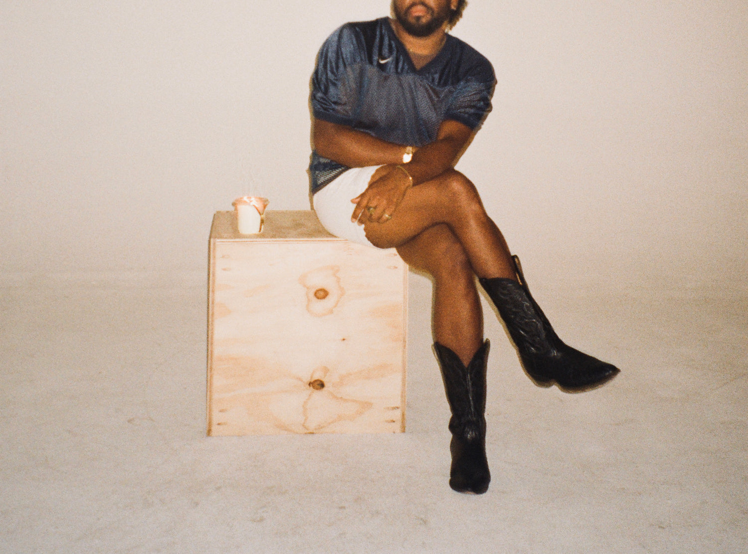 joseph ross sitting on a wooden box wearing a dark outfit and black boots circus candles spaces feature