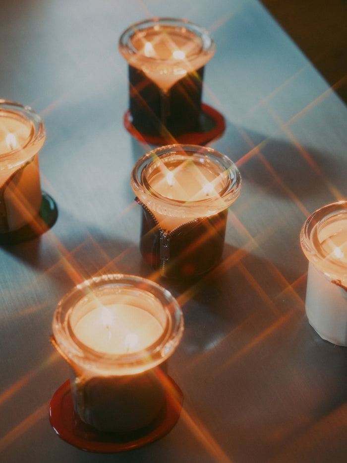 Zippered Circus candles lit on a steel table, starbursts of light crossing the glass