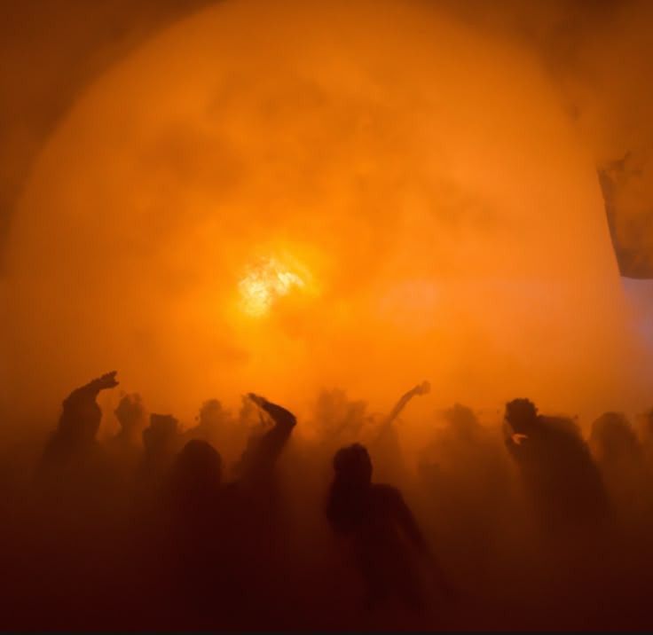 Silhouettes of people against a bright orange sky with a sun-like object