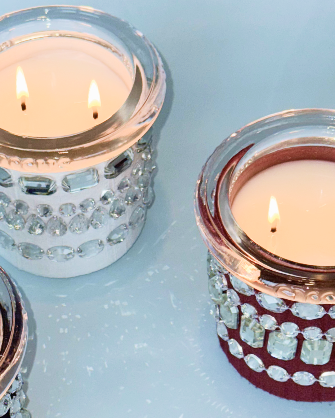 Two crystal fetish candles by circus gemstone pave accents on a light blue background.