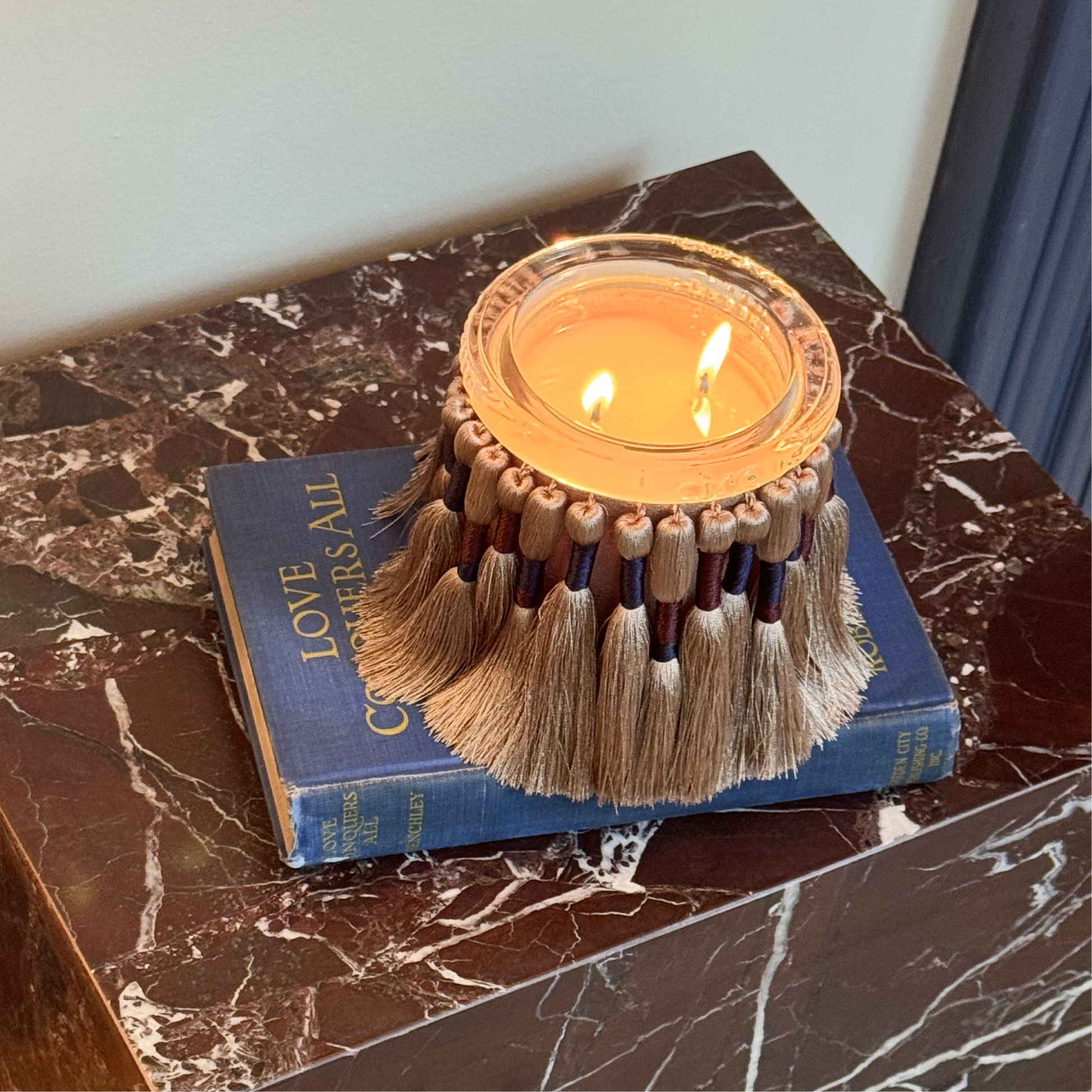 Candle by circus with tassels on a blue book on a marble surface