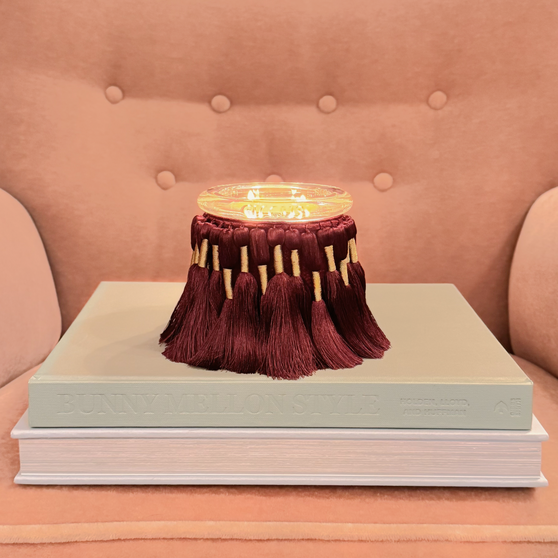 circus candle with tassels on a stack of books against a pink background