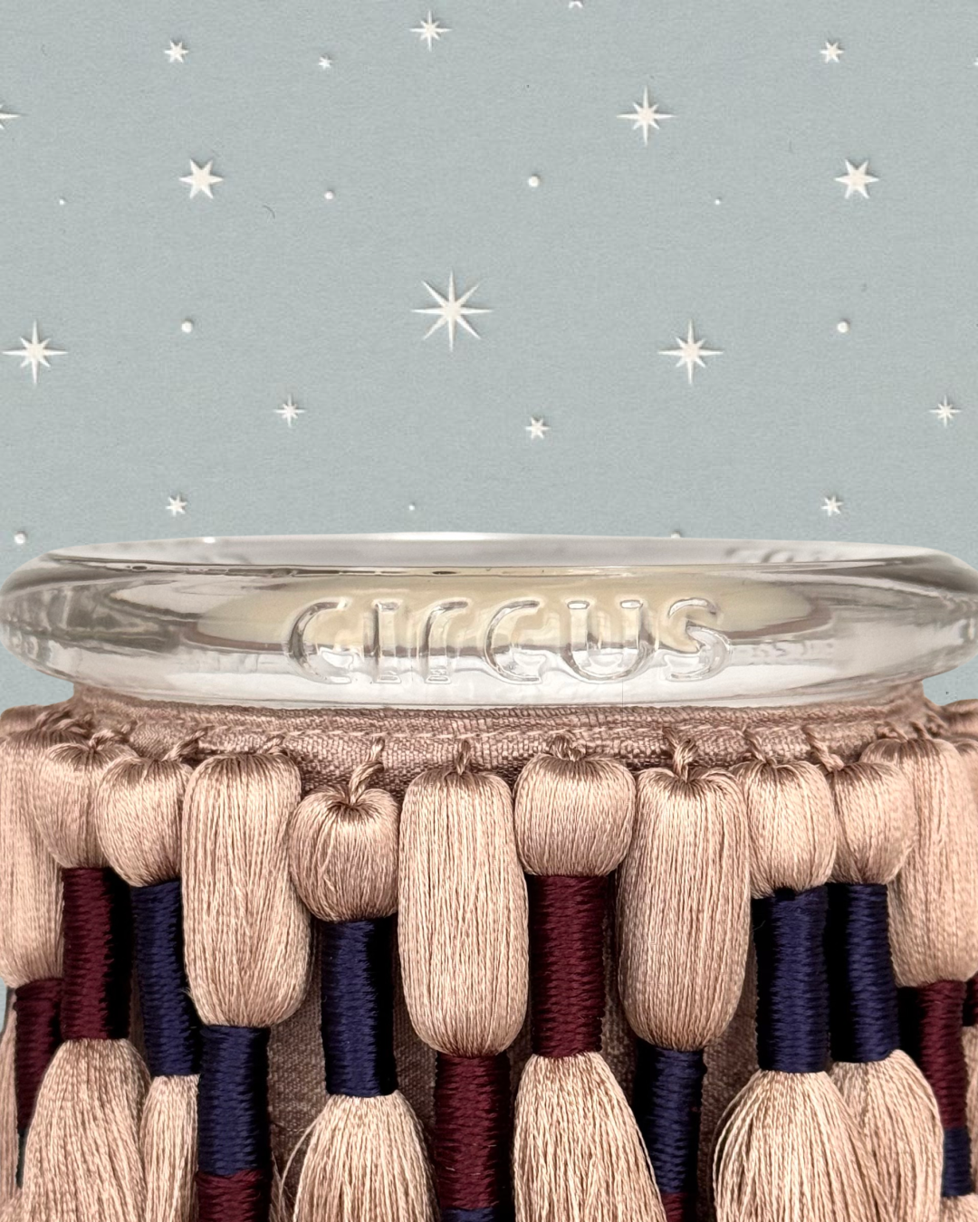 fuzzed candle by circus with silk tassels against a holiday star background